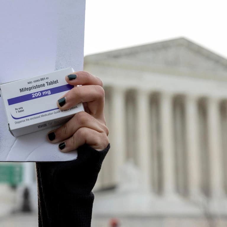 U.S. Supreme Court building exterior with mifepristone pill packaging and gavel in foreground